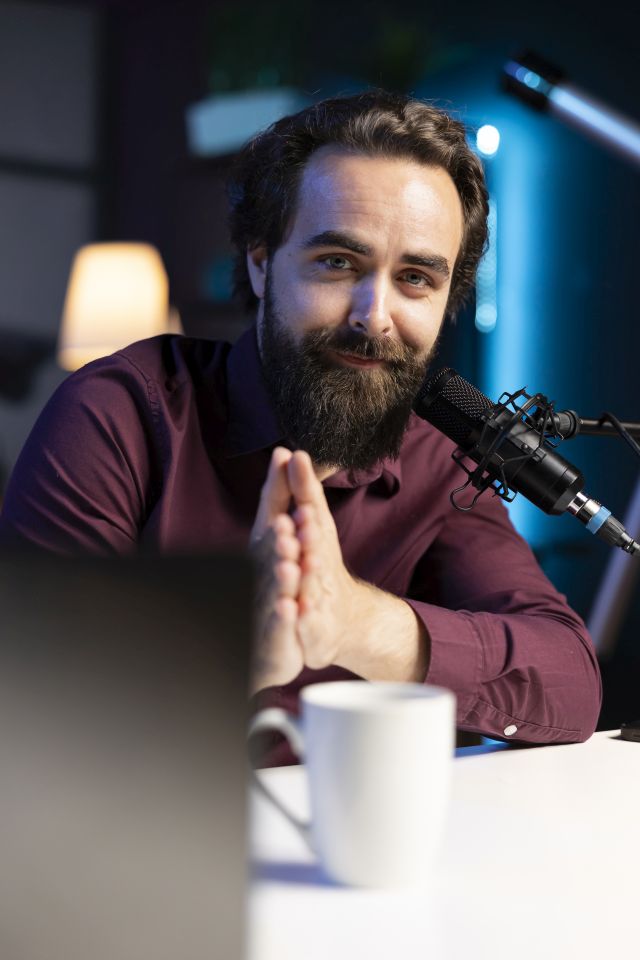 Portrait of smiling content creator hosting online show in rgb lights studio, shooting vlog using professional microphone. Cheerful vlogger presenting informations during streaming service broadcast
